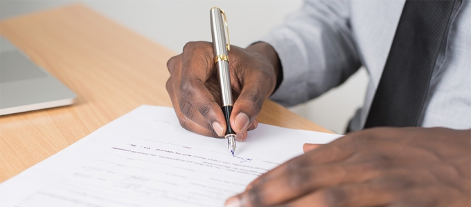 Person holding pen signing a form on white paper
